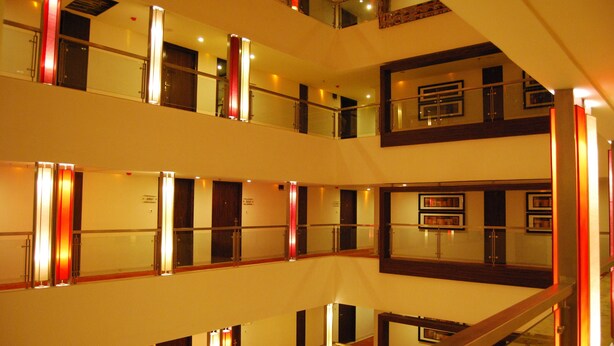 A multi-level hotel interior with glass railings, wooden accents, and multiple doors. - Royal Park (Kakinada)
