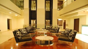 A spacious lobby with a central seating area featuring black leather sofas with patterned cushions, surrounded by glass-top coffee tables. - Royal Park (Kakinada)