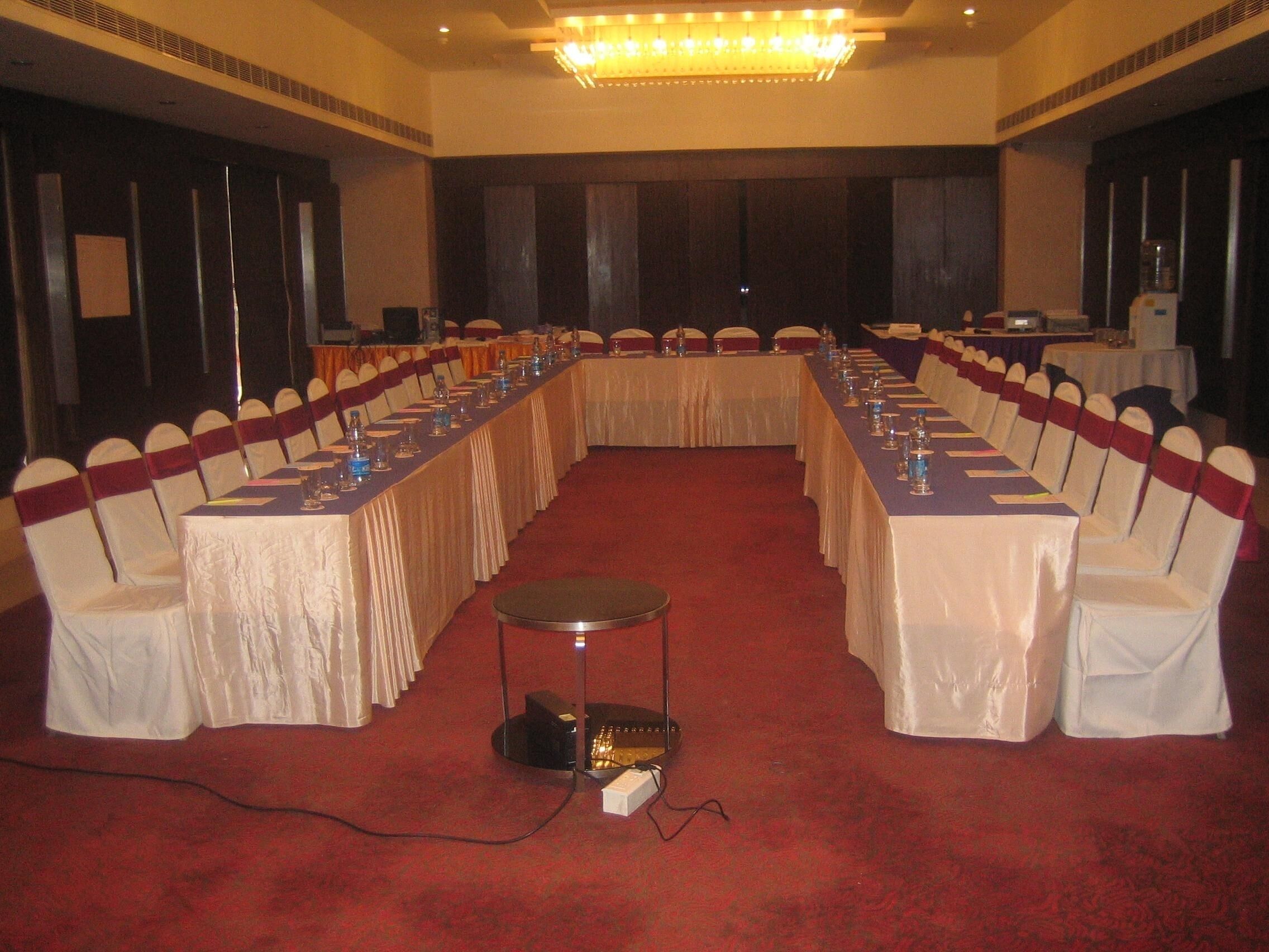 A conference room with a long table, chairs with white and red sashes, and a carpeted floor.