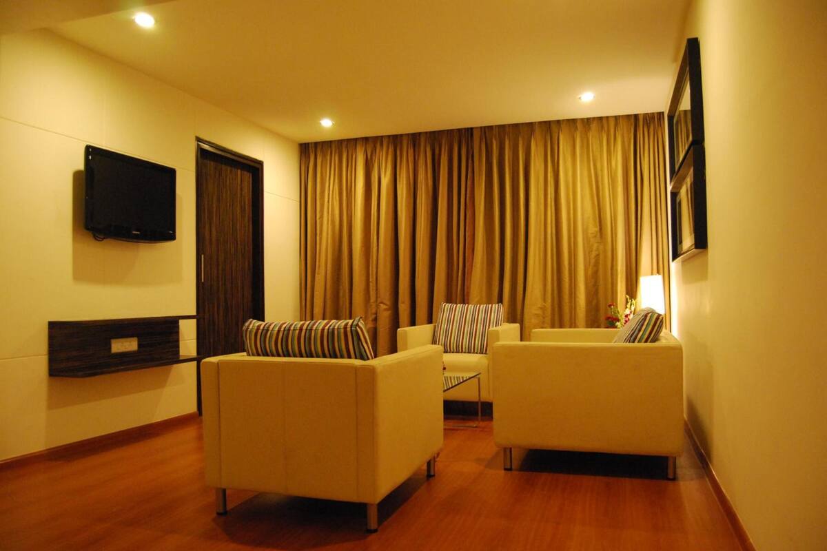 A hotel room with two sofas, a flat-screen TV mounted on the wall, and a large window with curtains.