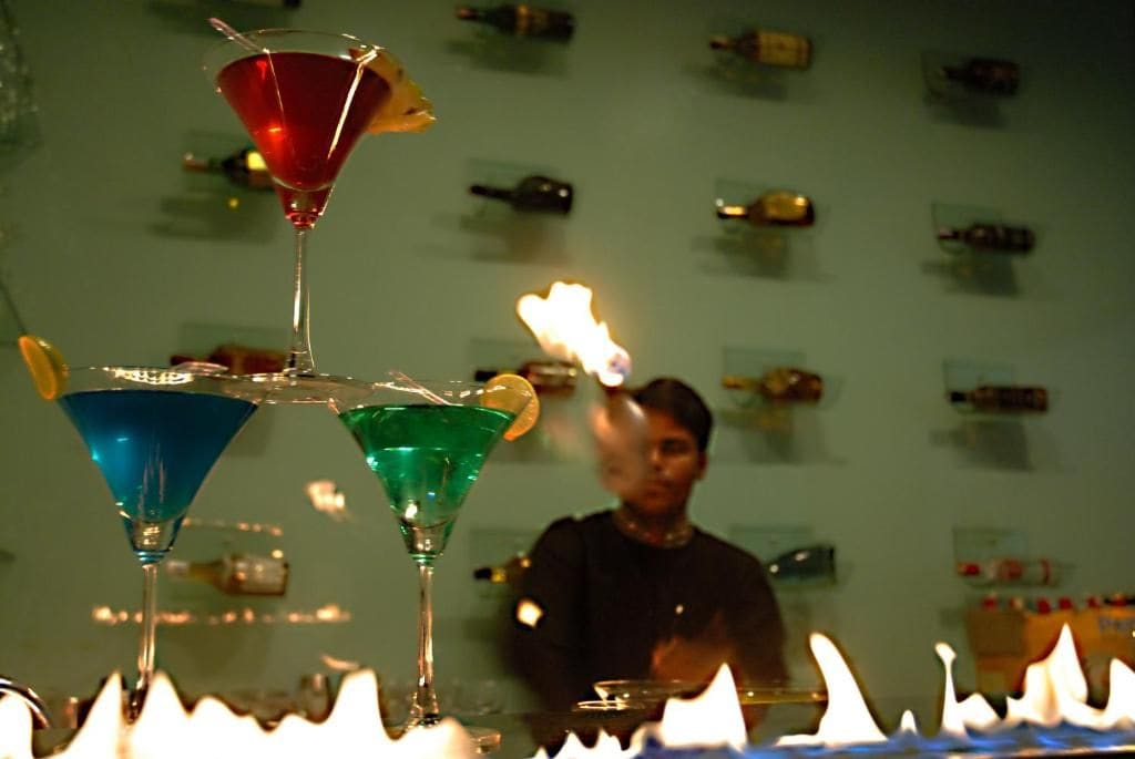 Angolo bar con bicchieri infuocati e bottiglie disposte sugli scaffali sullo sfondo.