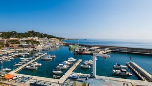 A marina with multiple boats docked, a lighthouse, and a coastal town in the background. - Hostal Port Corona (Capdepera)