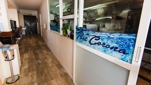 A corridor with a kitchen area visible through a glass partition. - Hostal Port Corona (Capdepera)