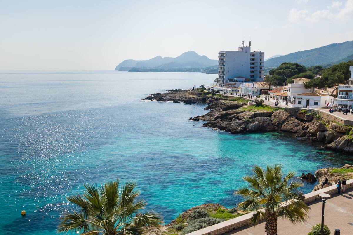 Un pueblo costero con mar azul cristalino, costa rocosa y edificios a lo largo de la orilla.