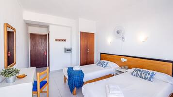 A hotel room with two beds, a desk, a chair, a mirror, a wall-mounted fan, and a small plant.