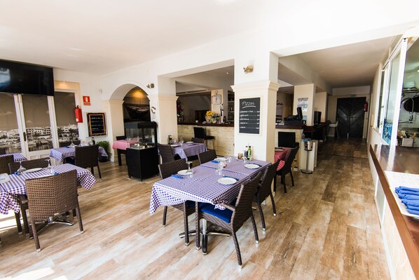 Un restaurant avec des nappes à carreaux, des chaises en osier et une vue sur la ville grâce à de grandes fenêtres.