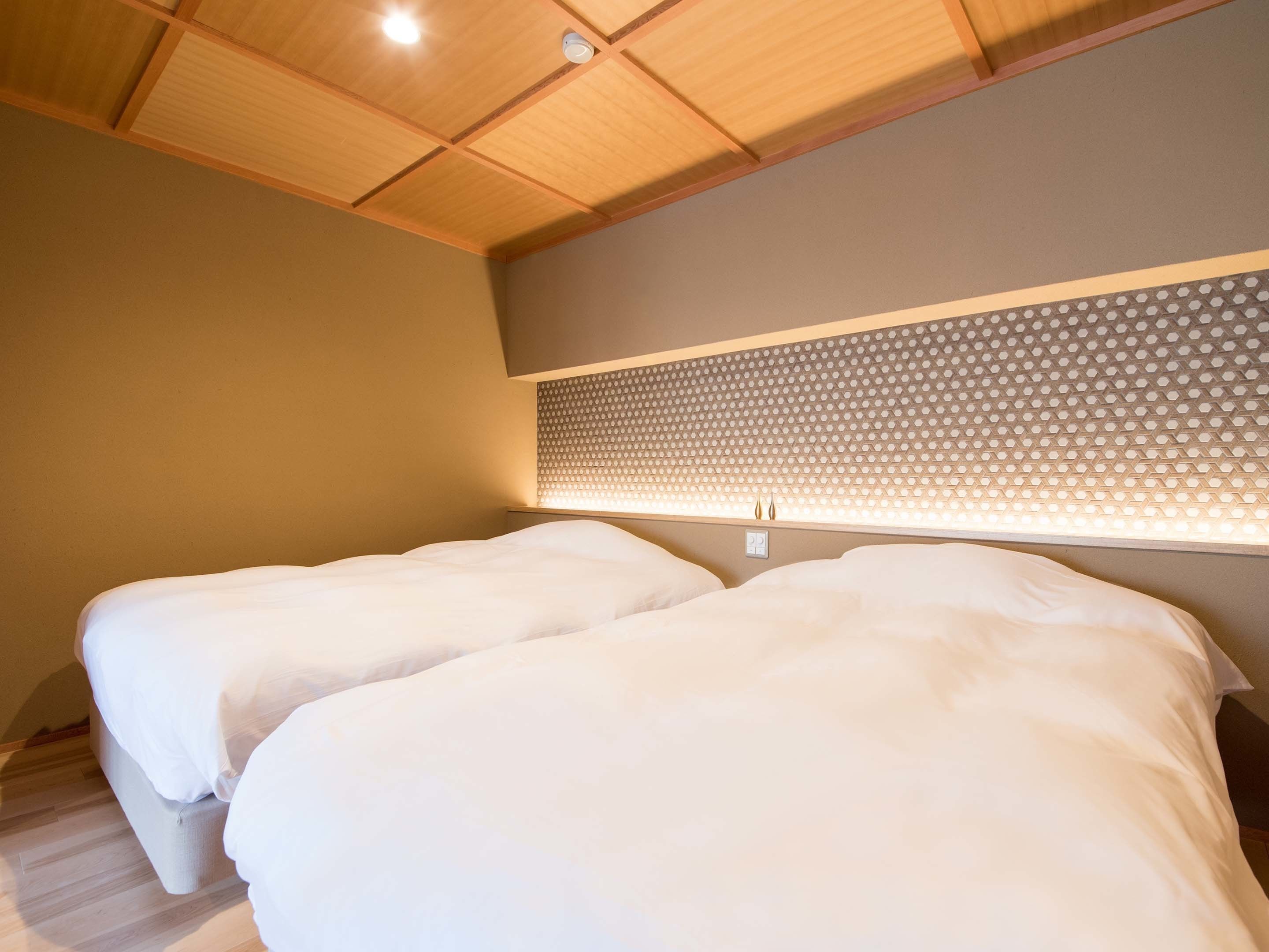 A bedroom with two beds, wooden ceiling, and a patterned wall headboard.