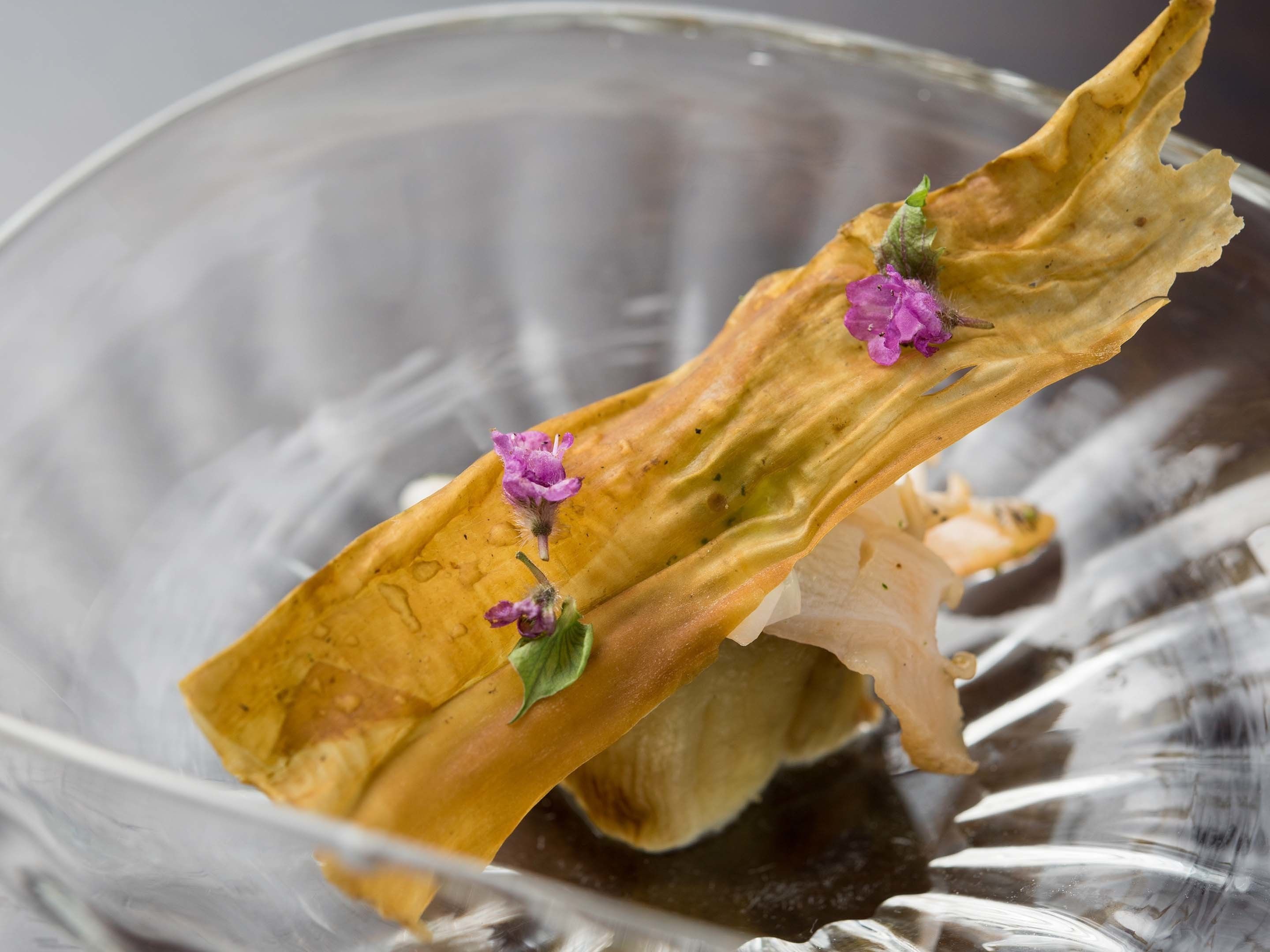 A clear glass bowl containing a dried plant with purple flowers.
