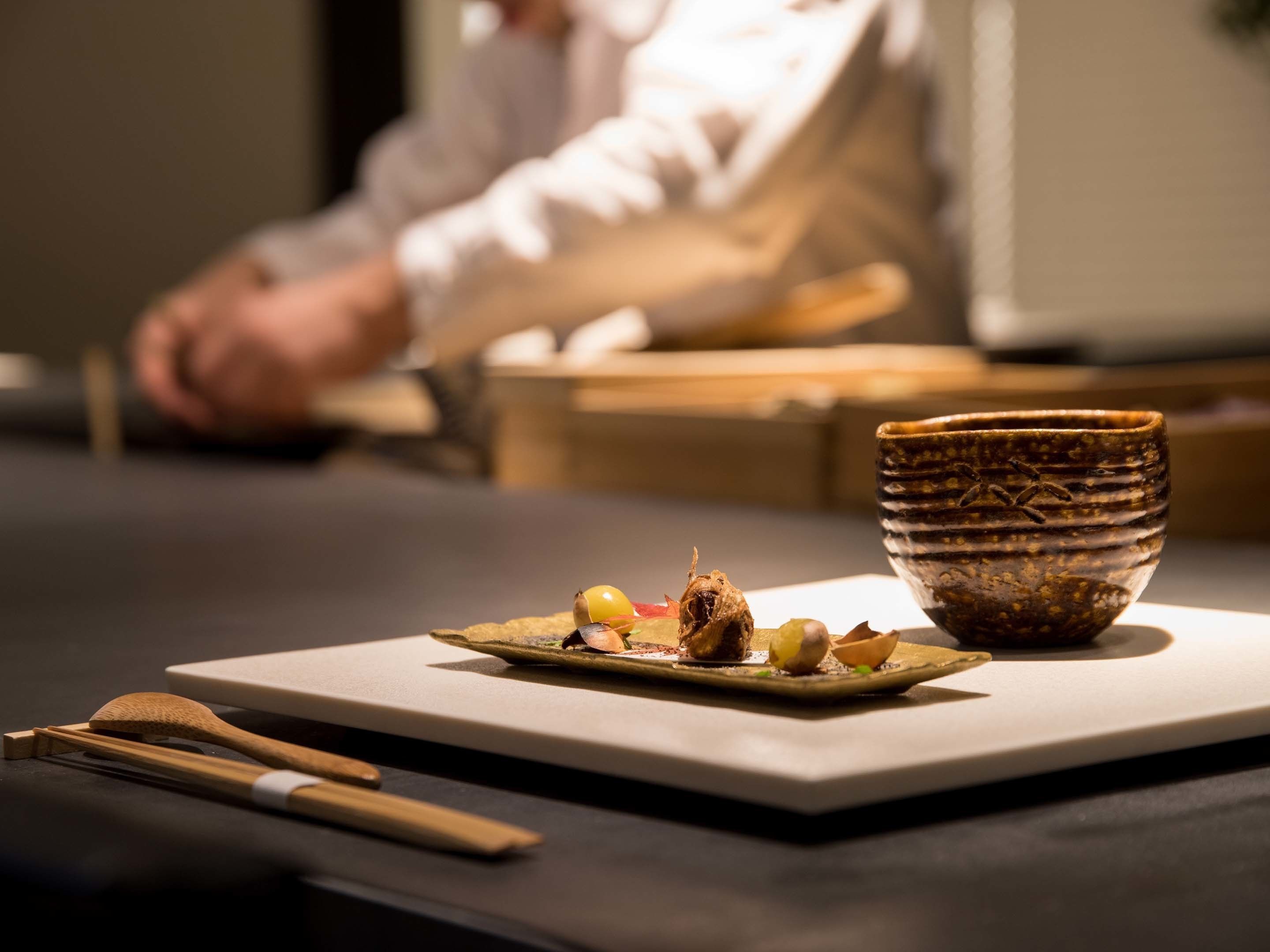 A dining table with a plate of food, chopsticks, and a ceramic bowl.