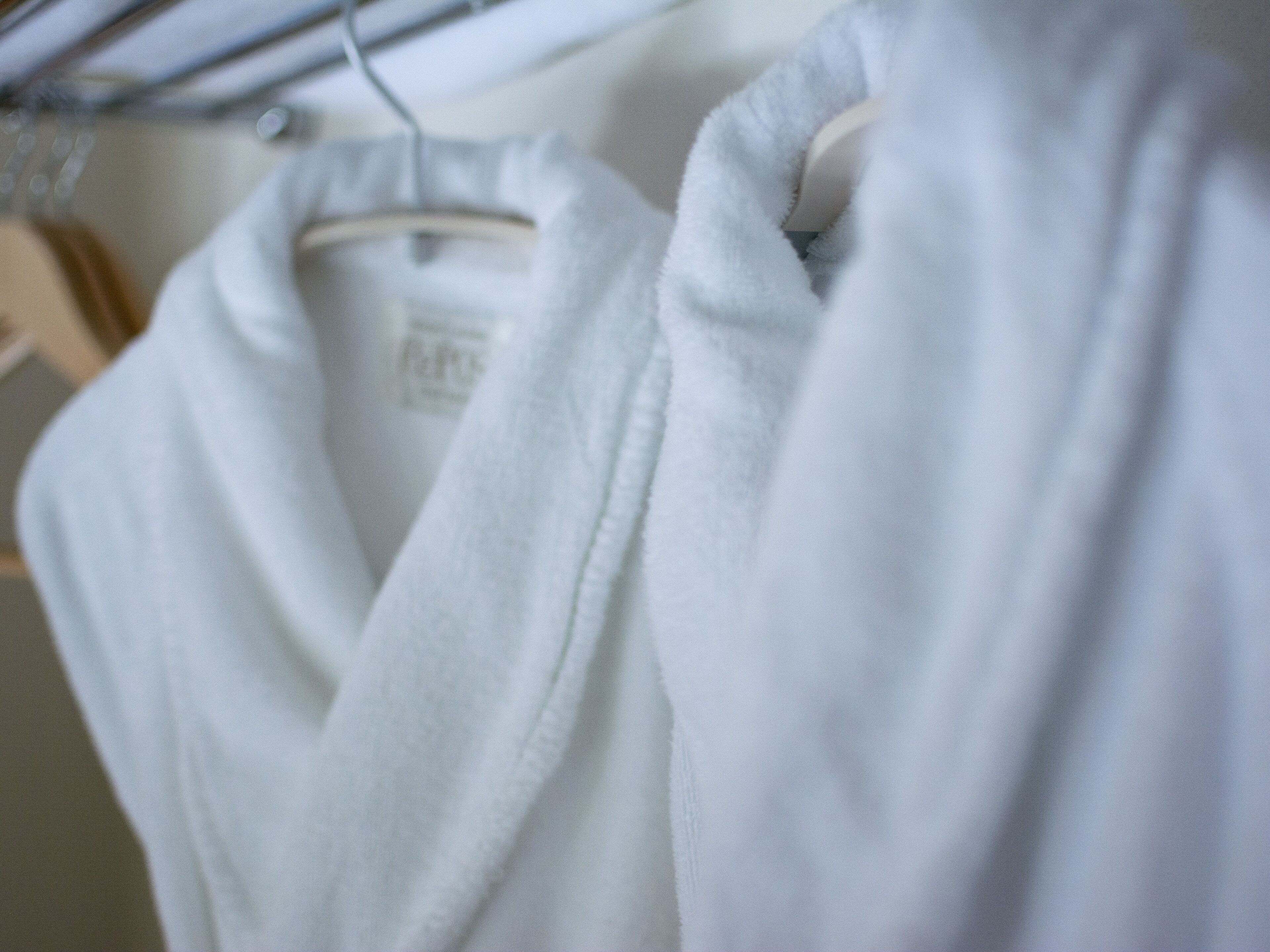 A white robe hanging on a wooden hanger.