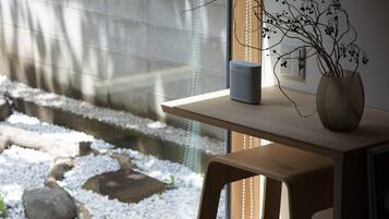 A room with a wooden table, a vase with branches, and a speaker on the table.