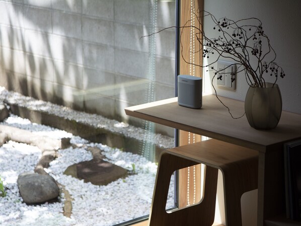 A room with a wooden table, a vase with branches, and a speaker on the table.