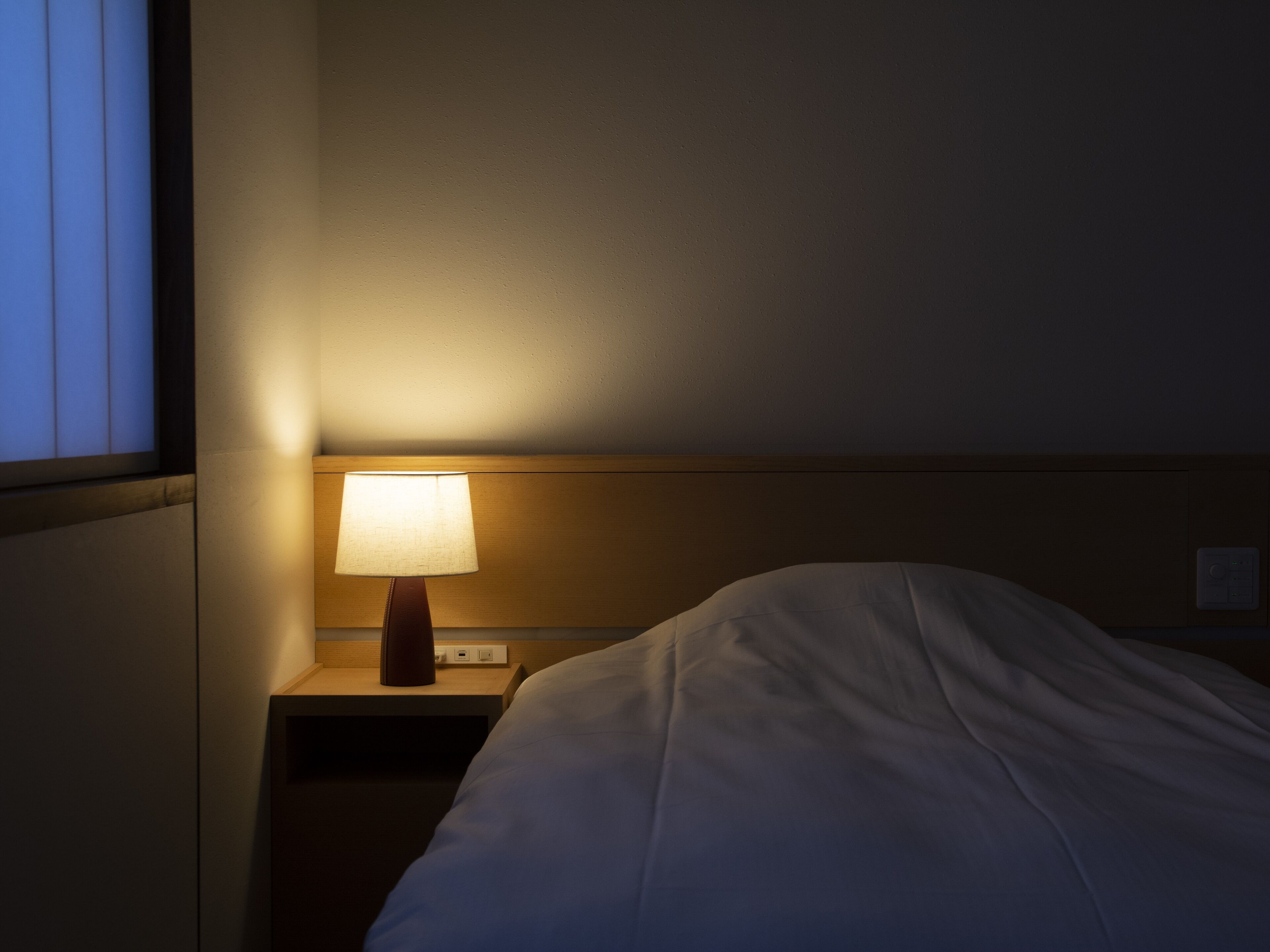 A hotel room with a single bed, a nightstand, and a bedside lamp.