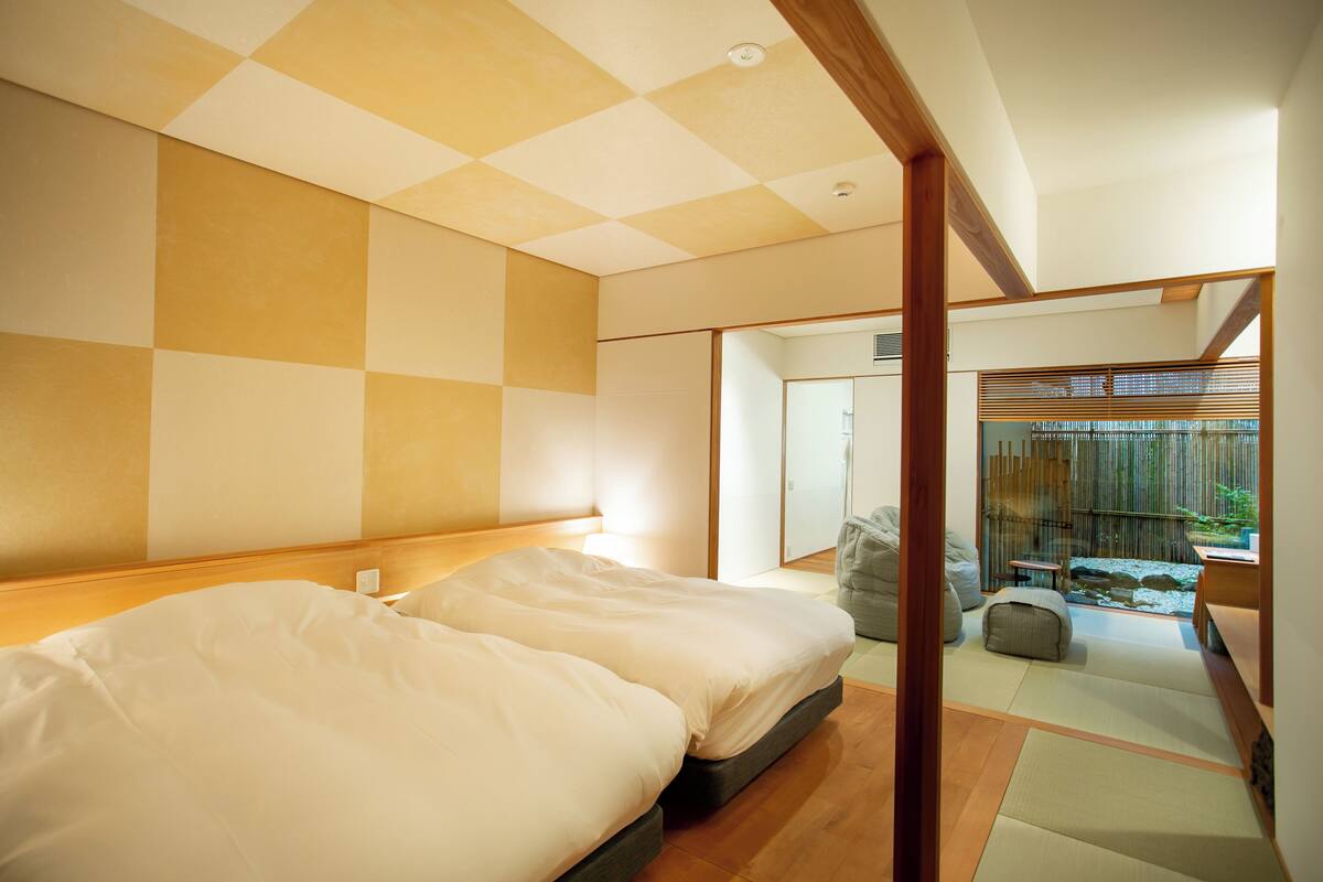 Une chambre d’hôtel avec deux lits, un plafond en bois et une vue sur un jardin, accessible par une porte coulissante.