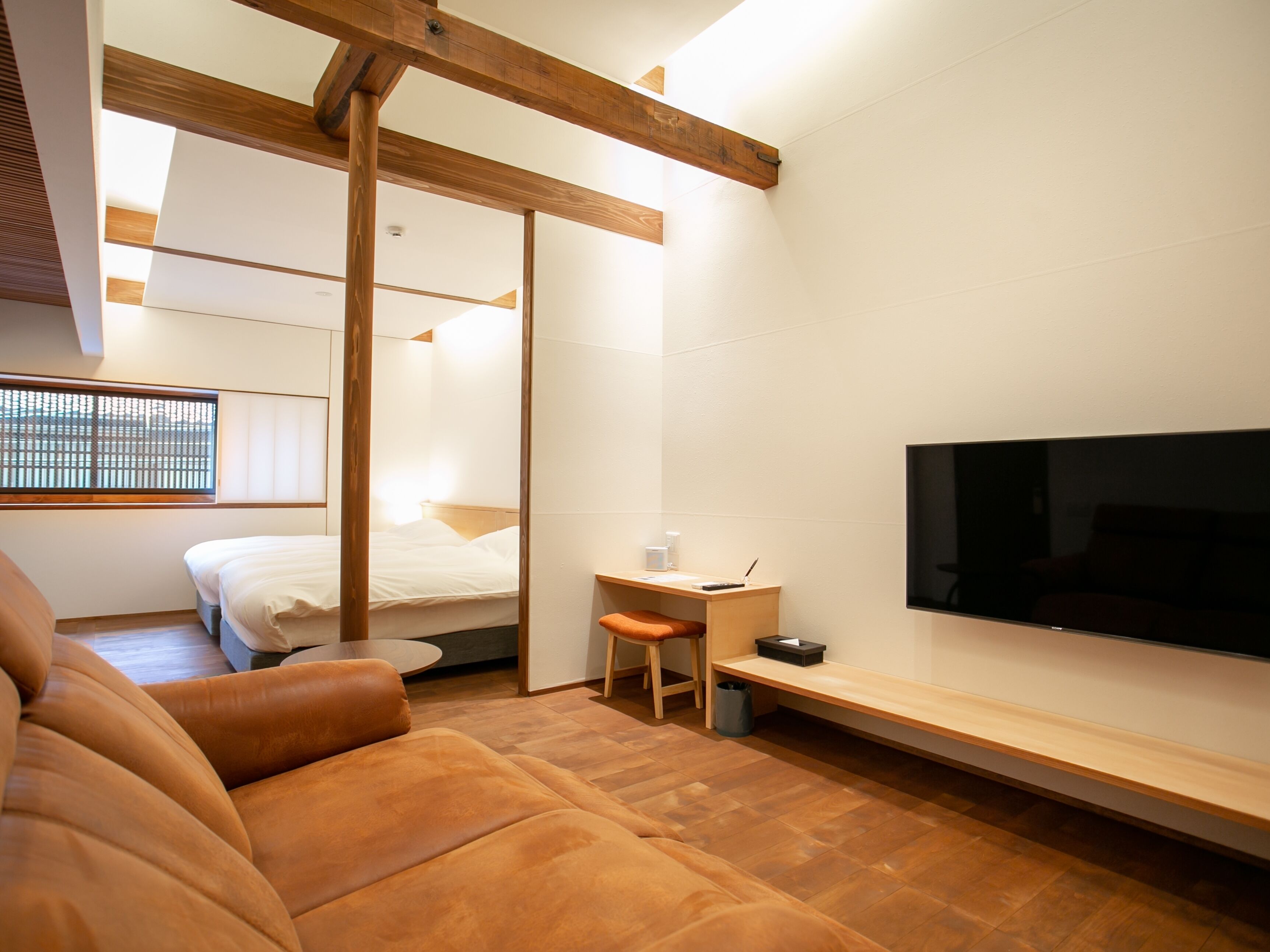 Camera d'albergo moderna con soffitto in legno, un letto grande, una scrivania con sedia, una TV e un divano.