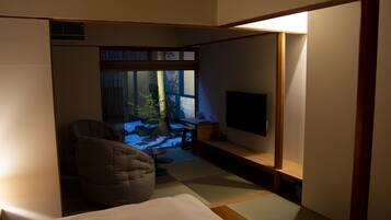 A room with a bed, a seating area with a chair, a television, and a view of a garden through a window.