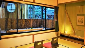 Een traditionele Japanse kamer met tatami vloerbedekking, een lage tafel met kussens, een schuifdeur met uitzicht op bamboe en een hangende scroll.