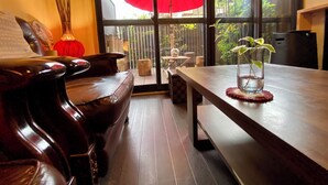 Een kamer met een houten tafel, een bank en een groot raam, buiten staat een rode paraplu.