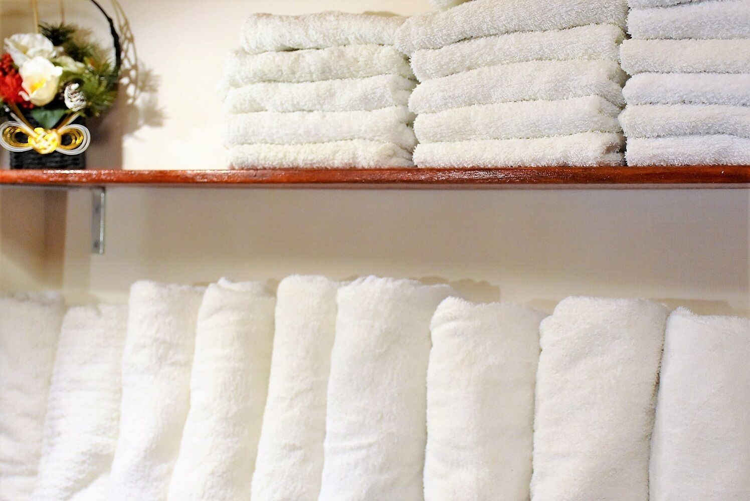 Neatly folded white towels stacked on a wooden shelf and hanging on a wall.