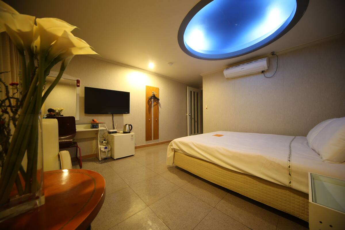 A hotel room with a bed, a desk, a chair, a television, and a ceiling light.