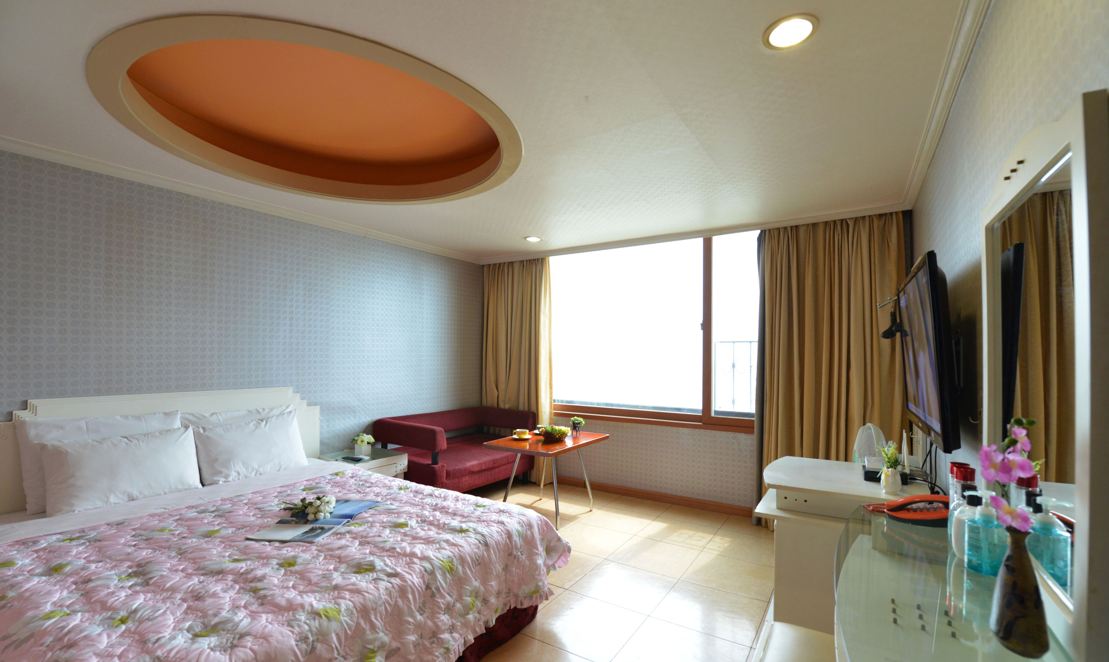 A hotel room with a large bed, a desk, a chair, a TV, and a window with curtains.