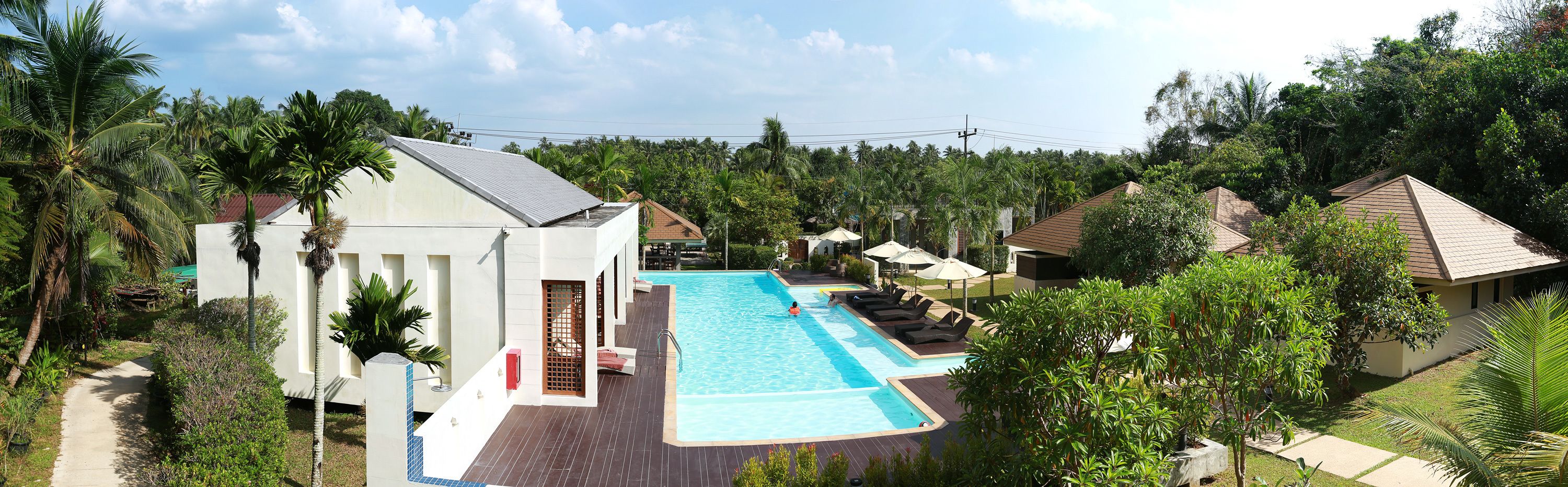 A resort with a large swimming pool, palm trees, and multiple bungalow-style buildings.