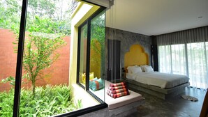 Un dormitorio moderno con un ventanal grande, una cama con cabecera y una pequeña zona de estar con cojines.