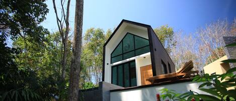 A modern house with a large glass window, surrounded by trees.