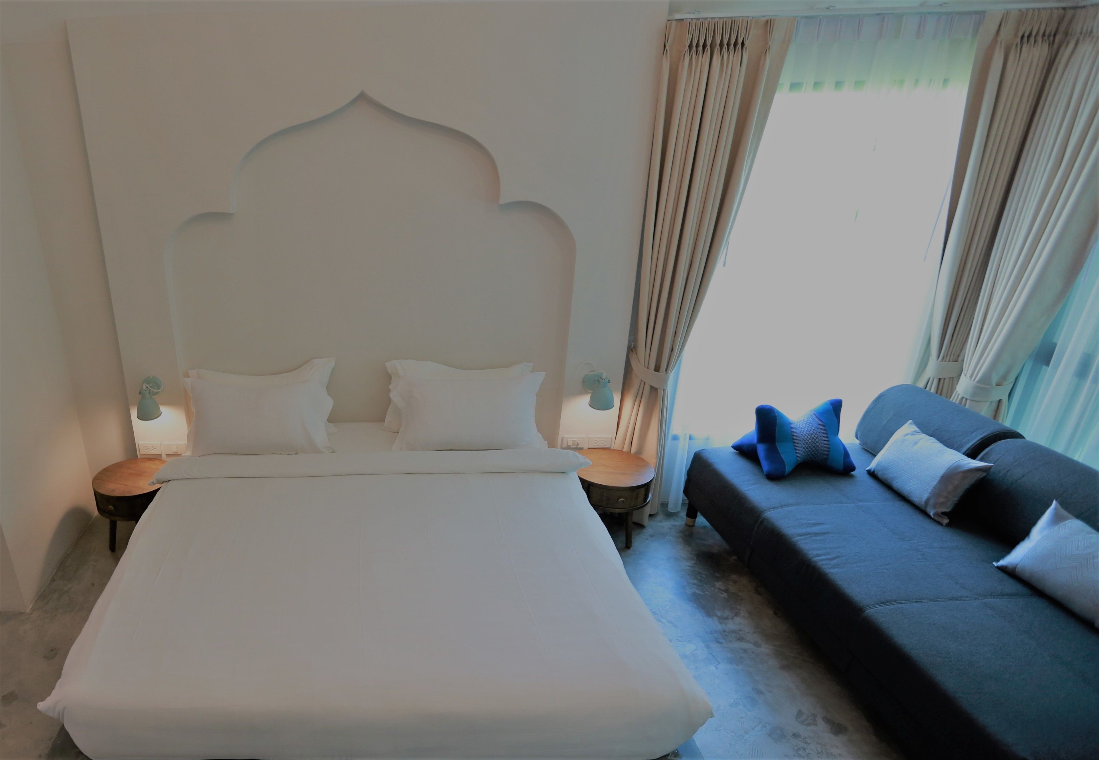 Un dormitorio con una cama grande, un sofá oscuro y una mesita de noche con lámpara.