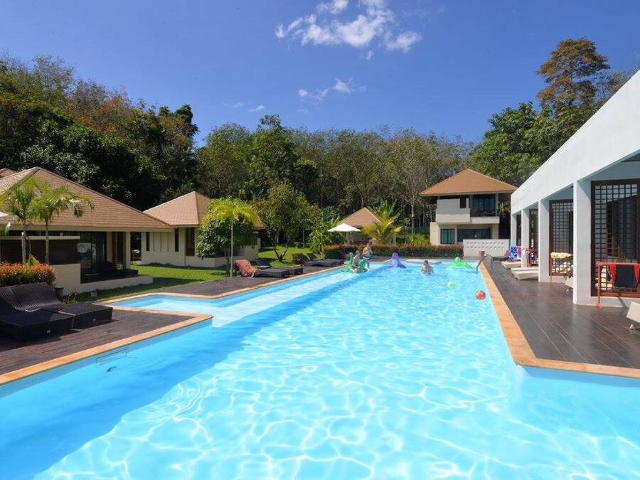 Una piscina con sillas de descanso y sombrillas, rodeada de edificios y vegetación.