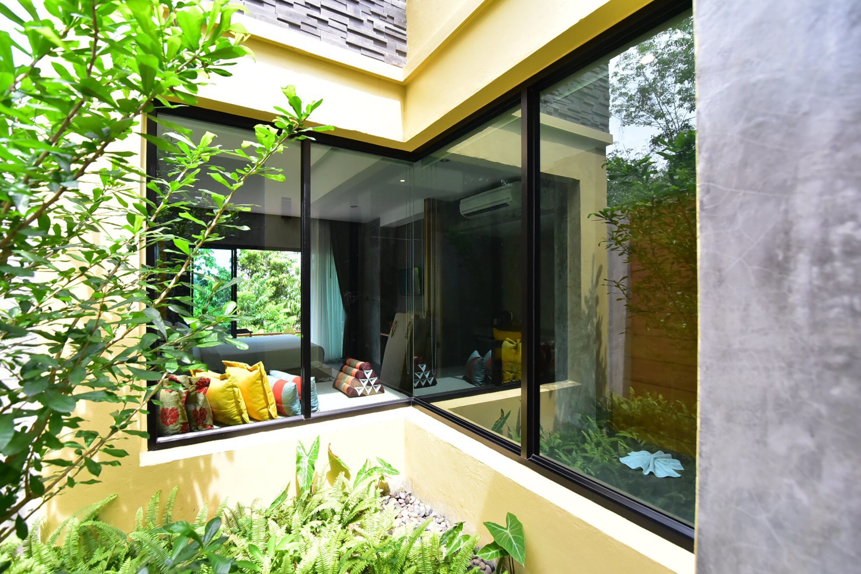 A corner room with a large window, a built-in bench with cushions, and a small garden area with plants.