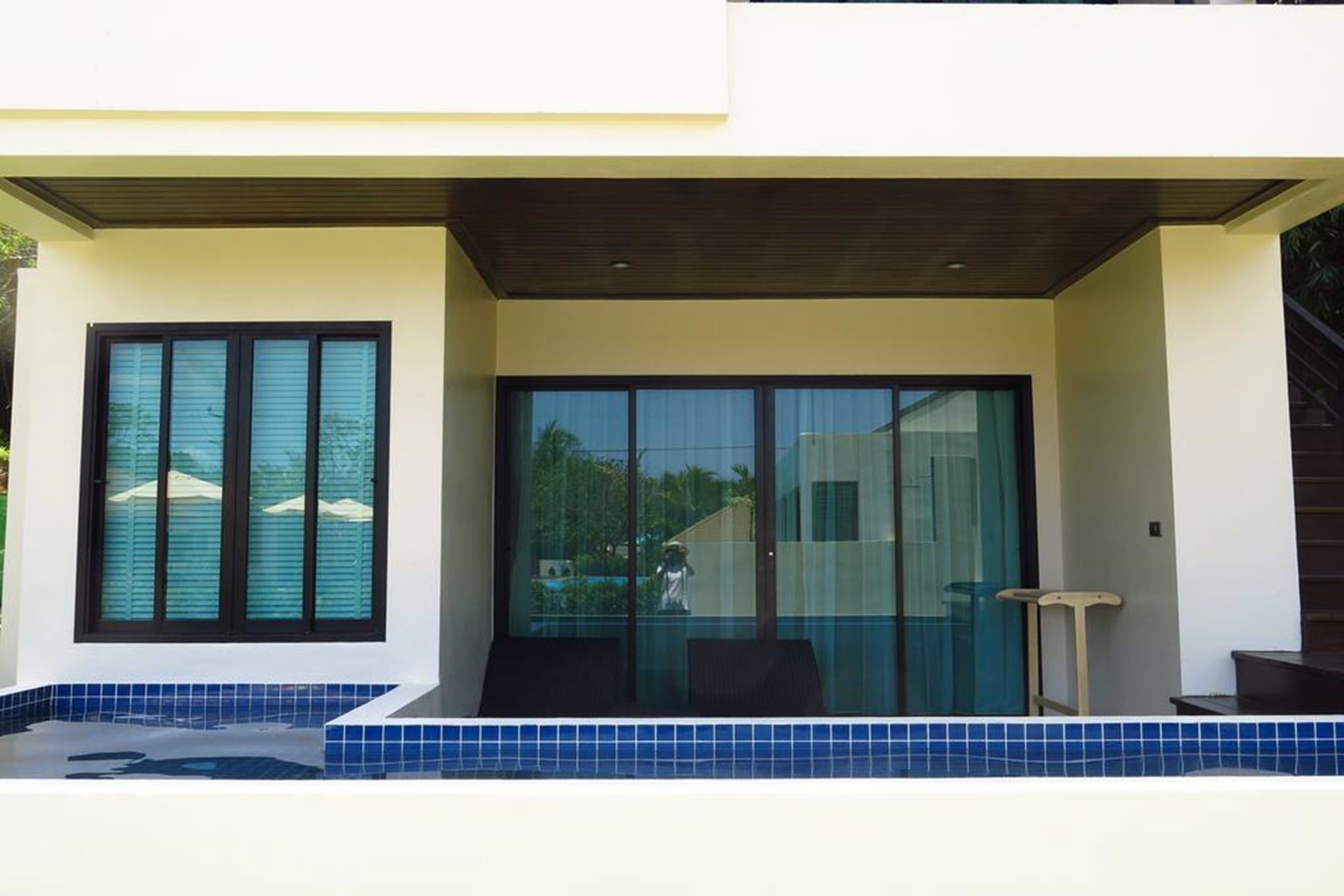 Un edificio moderno con un espacio exterior cubierto, puertas de vidrio amplias y una piscina con baldosas azules.