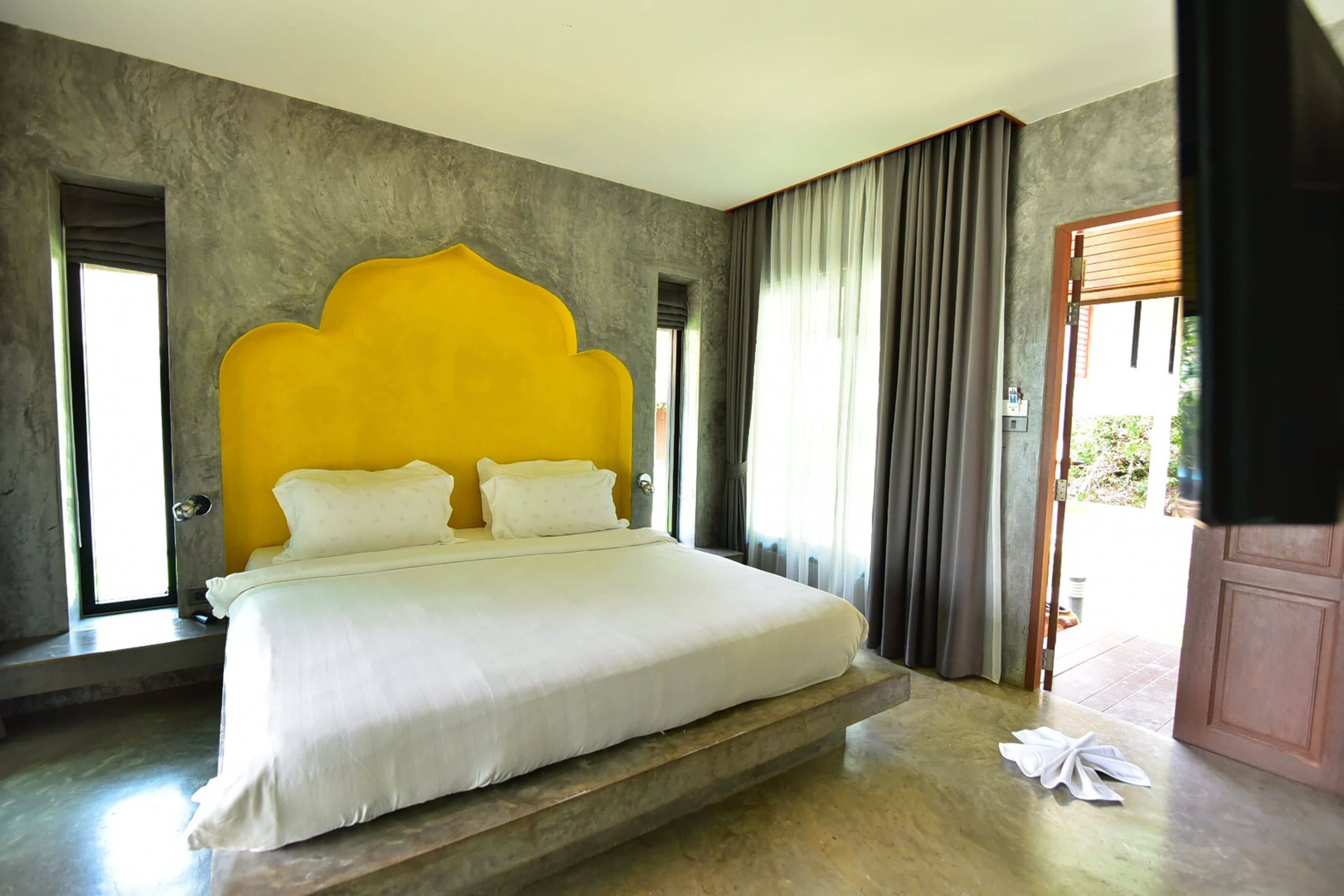Un dormitorio con una cama grande, un cabecero amarillo singular y vistas al exterior.