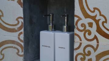 A bathroom with a shower gel and shampoo dispenser in a tiled alcove.