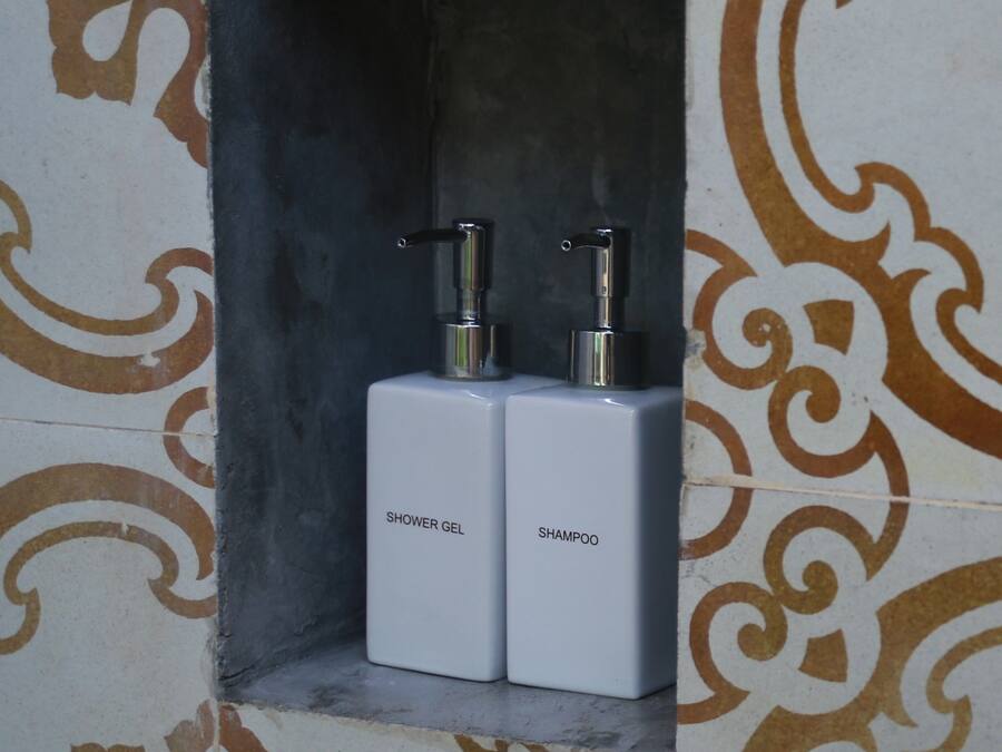 A bathroom with a shower gel and shampoo dispenser in a tiled alcove.
