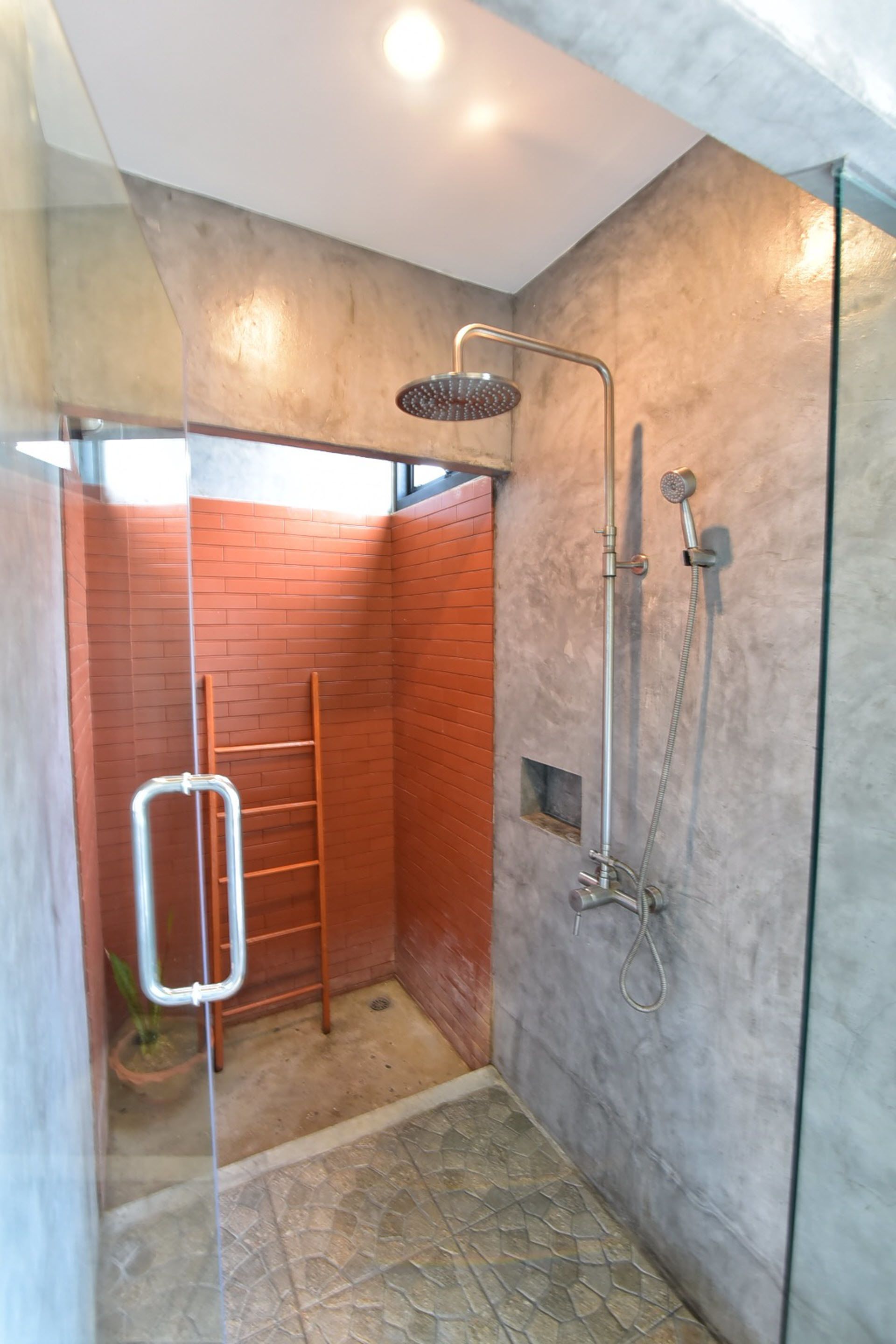 A modern shower area with a glass partition, a metal ladder, and a showerhead.