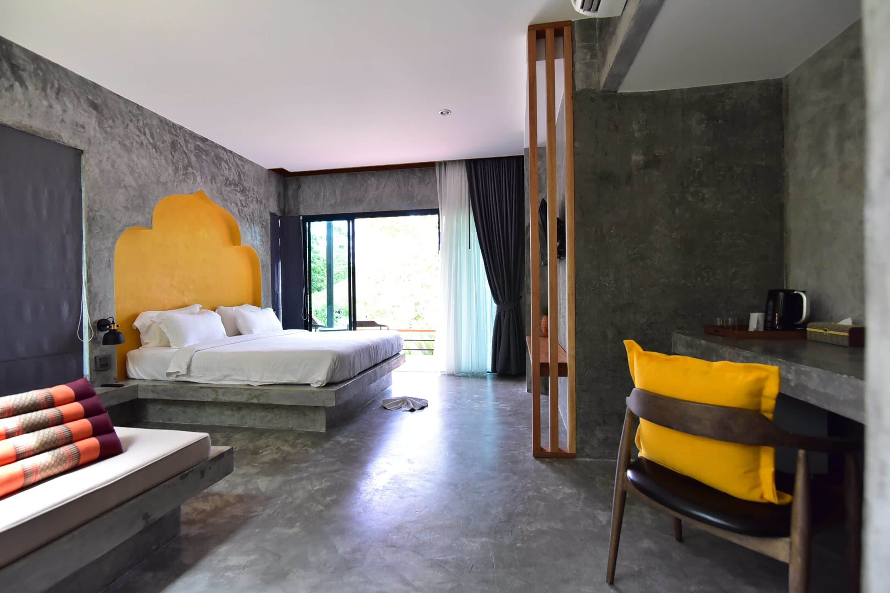 A modern bedroom with a large bed, a seating area with a chair, and a view of the outdoors.
