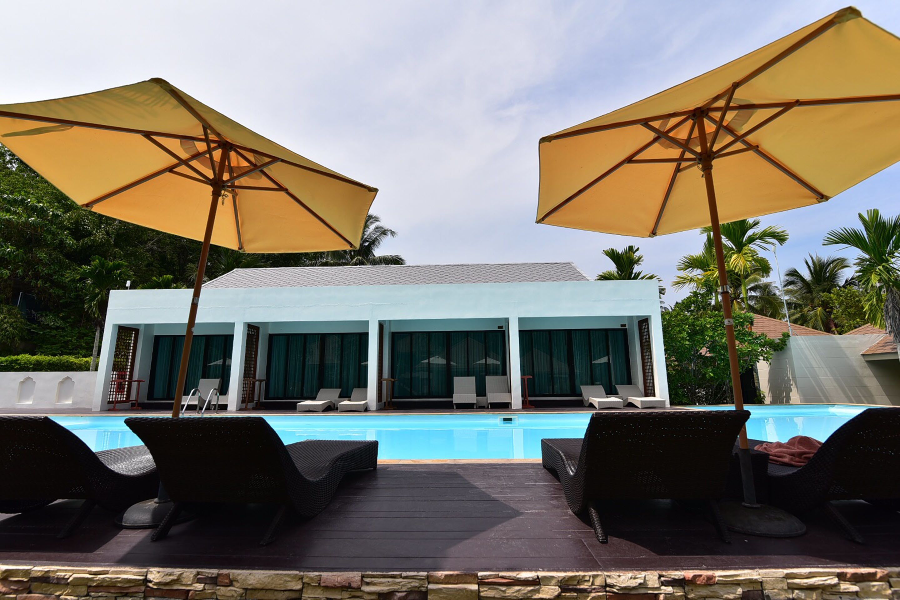 A poolside area with lounge chairs and umbrellas, a pool, and a building with large windows and curtains.