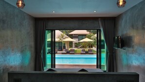 Un baño moderno con un ventanal grande, una bañera y vistas a una zona de piscina con sombrillas.
