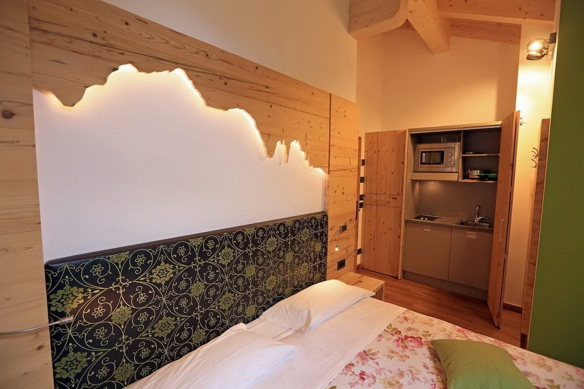 Ein Schlafzimmer mit Bett, Wandlampe und einer integrierten Küchenzeile.