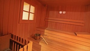 Ein Saunaraum mit Holzbänken, einem Fenster und einem kleinen Tisch mit einem Metallbehälter und einem Wasserschöpflöffel.