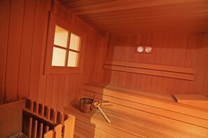 Een sauna met houten banken, een raam en een tafeltje met een metalen bak en een opscheplepel.