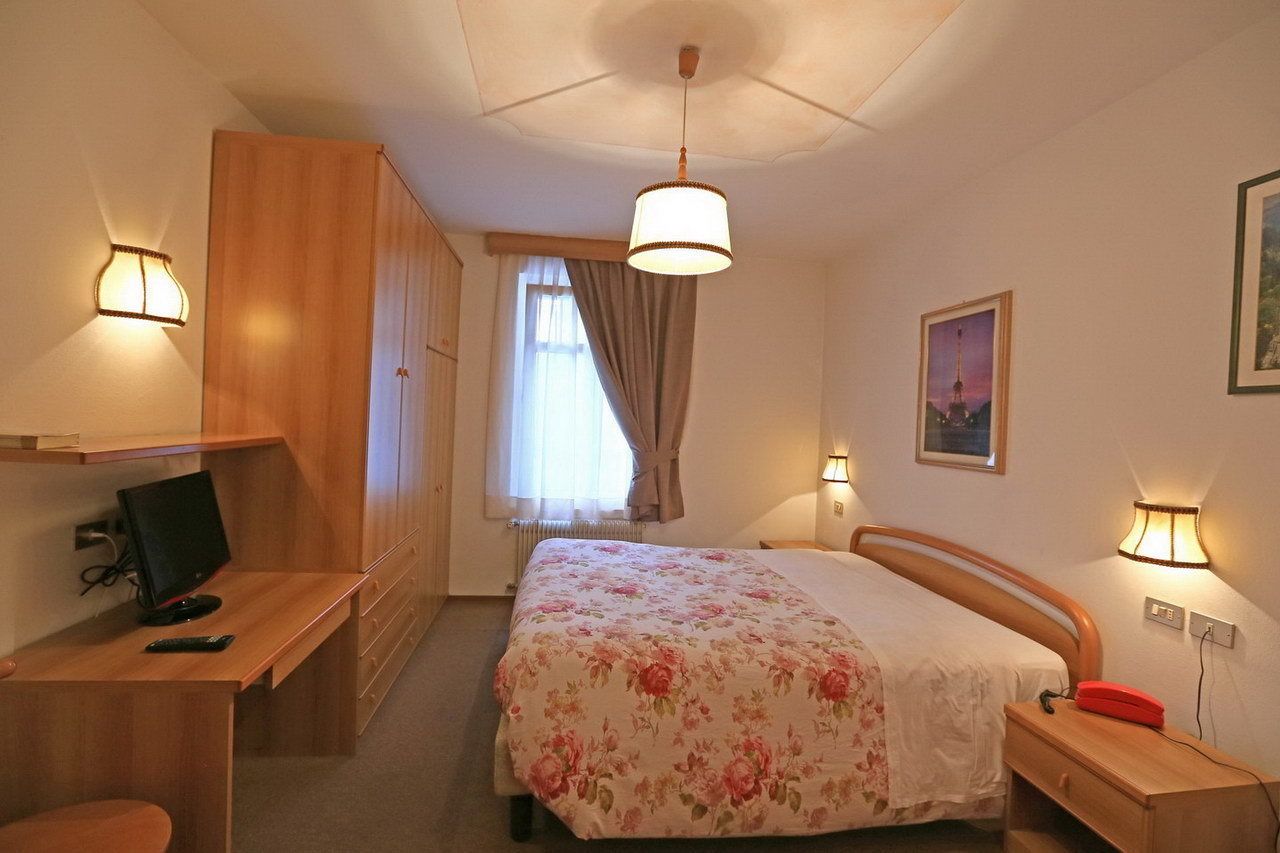 A bedroom with a bed, a desk, a chair, a wardrobe, and a window with curtains.