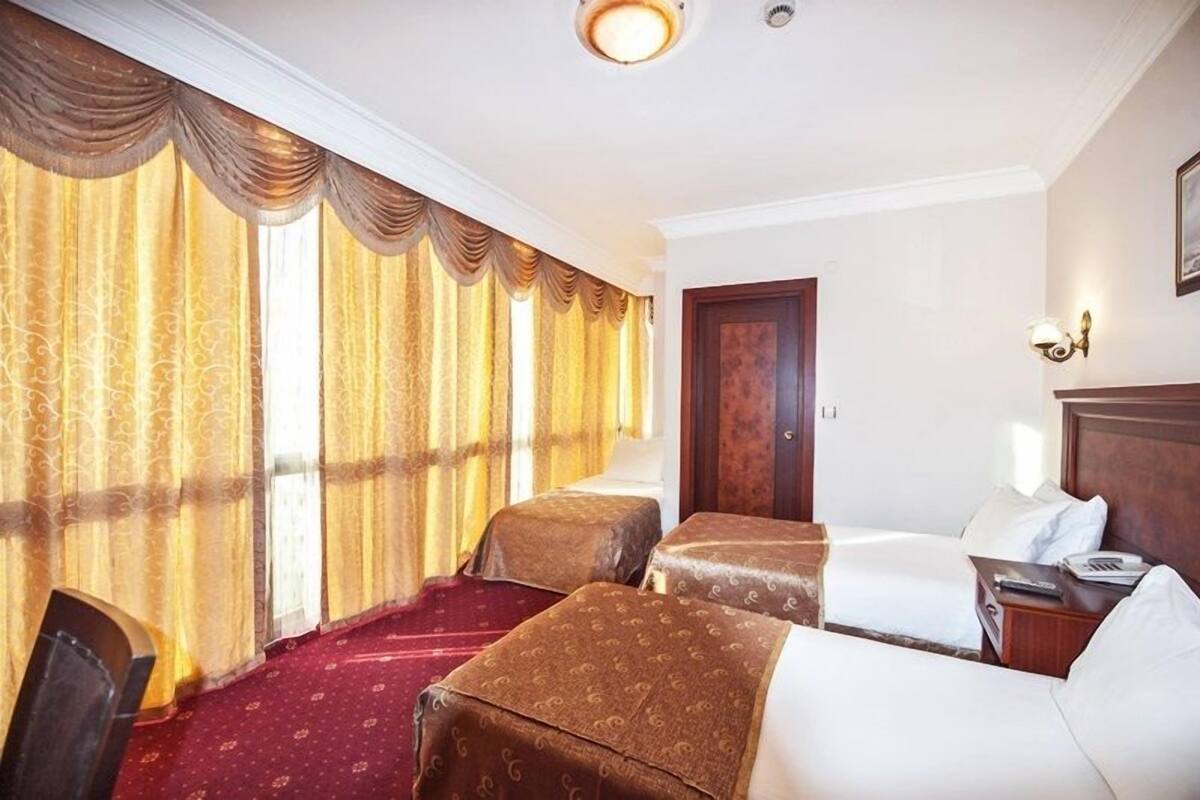 A hotel room with two beds, a wooden door, a red carpet, and a nightstand with a lamp.