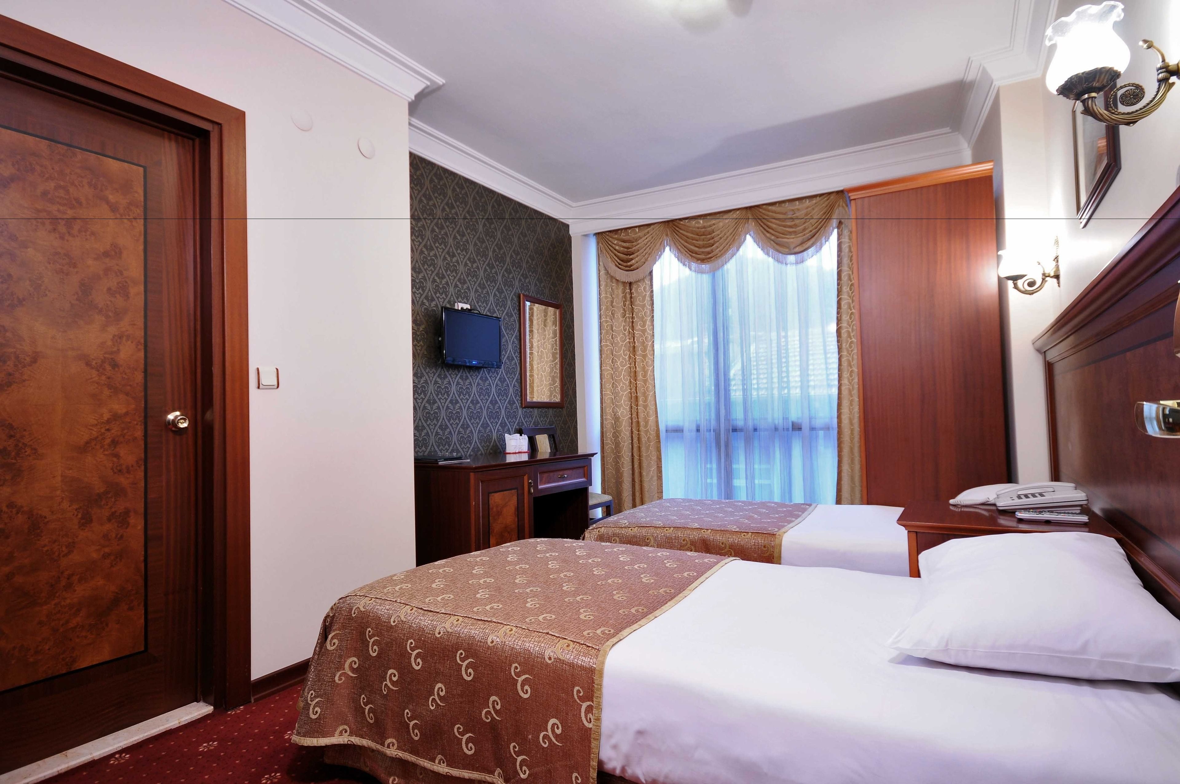 Camera d'albergo con due letti, una scrivania, una televisione e un'ampia finestra con tende.