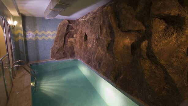 An indoor swimming pool with a rocky wall, metal handrails, and a tiled floor. - Grand Eyuboglu Hotel (Istanbul)