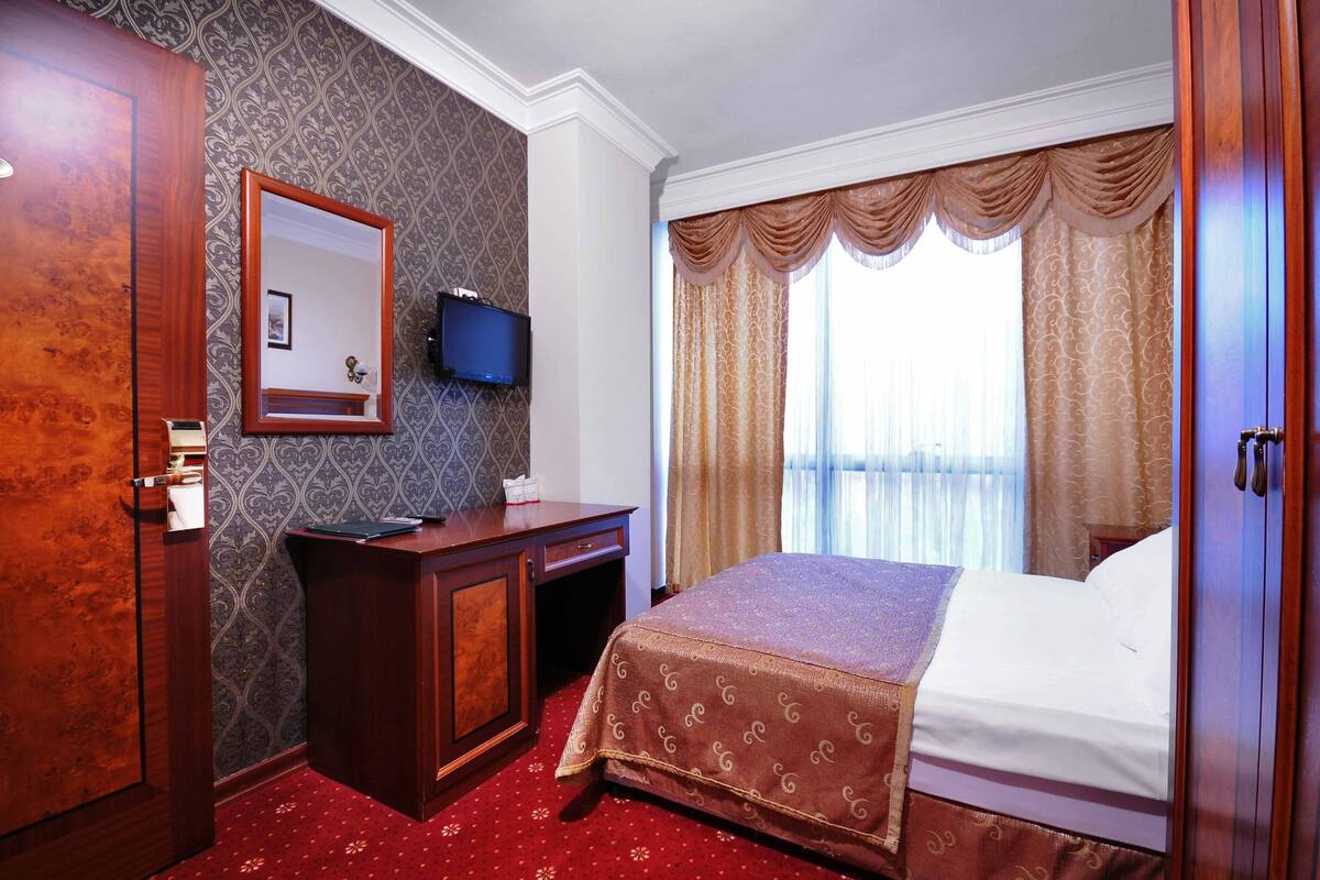 A hotel room with a bed, a desk, a television, and a wardrobe.
