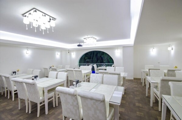 A dining area with white tables and chairs, a chandelier, and a large window with a view of trees. - Grand Eyuboglu Hotel (Istanbul)