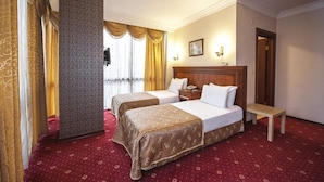 A hotel room with two beds, a wooden headboard, a bedside table, a red carpet, and a large window with curtains. - Grand Eyuboglu Hotel (Istanbul)