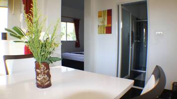 A room with a white table, a brown vase with a plant, a bed with white bedding, and a door leading to another room.